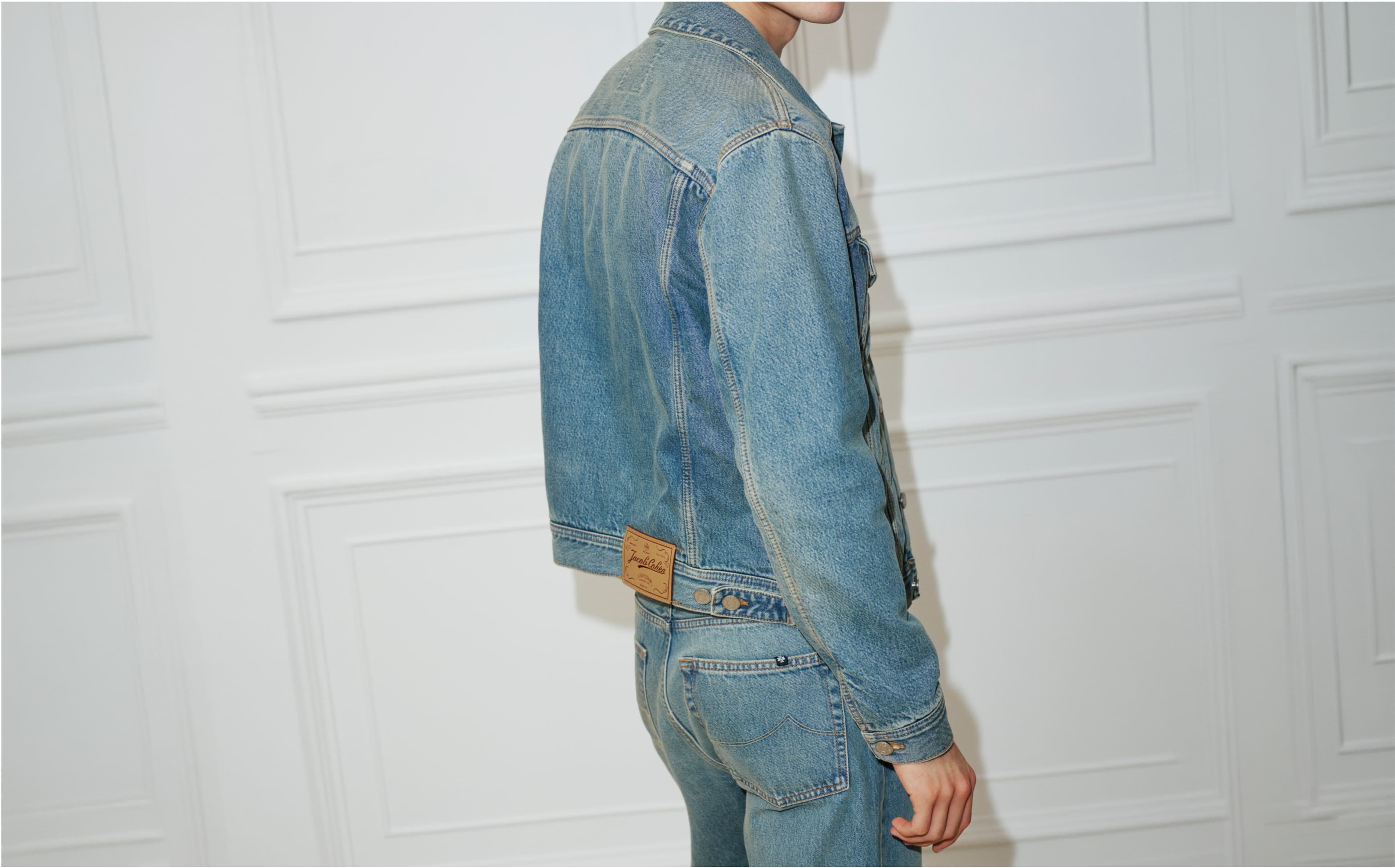 Shop denim — denim jacket and jeans worn against a panelled wall.